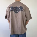 Remera boxy color marrón topo, de manga corta y corte holgado, con estampa en la espalda con la inscripción "MDW CLOTHING".