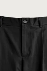 Pantalón relaxed fit de algodón color negro, con pliegues frontales en la cintura, bolsillos laterales y cierre frontal con cremallera y botón.