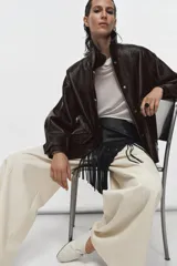 Chaqueta de cuero sintético con textura rugosa, cuello alto con trabilla, cierre frontal con cremallera y botones a presión, bolsillos delanteros y bajo ajustable con hebilla metálica.