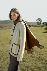 Cardigan de tejido de punto liviano con diseño de rayas verticales en tonos crema y amarillo. Presenta un cierre frontal estilo japonés con botones de nudo, bolsillos frontales y bordes contrastados en color marrón.
