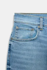 Jeans de mezclilla azul claro, tiro medio, corte recto y ligeramente acampanado en el bajo. Presenta cinco bolsillos y cierre frontal con cremallera y botón metálico.