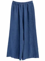 Pantalón azul jean de corte amplio y fluido, con cintura elástica fruncida y detalles de alforzas y costuras decorativas en los laterales.