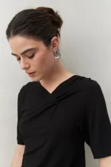 Remera negra de manga corta con escote asimétrico y detalle de nudo con frunces en el centro del busto.