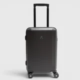 Valija de mano rígida color negro con acabado texturizado, diseño minimalista y logo frontal. Cuenta con cuatro ruedas giratorias y manija telescópica ajustable.