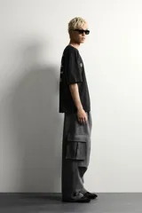 Pantalón jogger de corte relajado confeccionado en tejido de algodón compacto con elasticidad. Presenta cintura elástica ajustable con cordón, bolsillos laterales, bolsillos cargo con solapa en las piernas y detalle de pliegues en las rodillas.