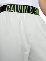 Short de dormir blanco de corte holgado, con cintura elástica negra que lleva el logo de Calvin Klein en verde neón.
