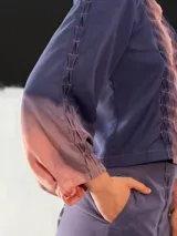 Chaqueta entallada de algodón tipo seda, teñida a mano con técnica tie-dye en tonos azul y naranja. Tiene cuello mao, mangas largas con puños abullonados y cierre frontal con broches.