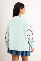 Buzo oversize de algodón con spandex, color verde menta, de manga larga con diseño de flores bordadas en rojo en las mangas y cuello redondo.
