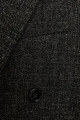 Abrigo largo de mujer, color gris oscuro jaspeado, con cuello solapa de muescas, manga larga y cierre cruzado con botones frontales. Presenta bolsillos con solapa en el delantero y aberturas en el bajo.