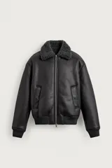 Cazadora oversize de efecto piel color negro, con interior y cuello solapa de pelo sintético gris a contraste. Cuenta con bolsillos de vivo en la cadera, acabados en rib elástico y cierre frontal con cremallera.