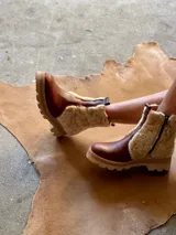 Botas de cuero marrón con la caña recubierta de corderito verde. Presentan una suela de plataforma tipo track en color beige y un tirador en la parte posterior para facilitar el calce.