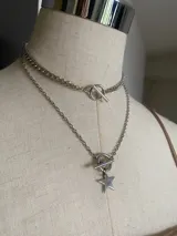 Conjunto de dos collares plateados. El collar superior es una gargantilla de cadena tipo eslabón cubano con cierre de palanca (toggle clasp). El collar inferior es una cadena más larga con un dije de estrella colgante, también asegurado con un cierre de palanca.