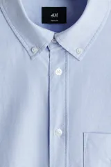 Camisa de algodón Oxford con cuello americano, bolsillo frontal y mangas largas con puños abotonados. Presenta un corte estándar y bajo redondeado.