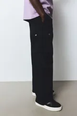 Pantalón cargo negro de corte holgado, con cintura elástica, bolsillos laterales, bolsillos tipo cargo con solapa y botón a presión en los laterales y bolsillos traseros con solapa y botón a presión.