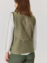 Chaleco de paño con diseño bicolor, frente en color negro y espalda en color marrón con textura de espiga. Presenta un maxi bordado de hoja en la parte posterior y detalles de tejido en los bordes.