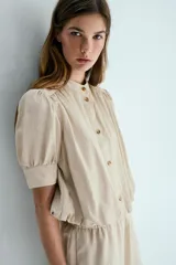 Blusa de sarga suave en color beige, con cuello mao, botonadura frontal con botones carey, mangas cortas abullonadas con puños y bajo globo.