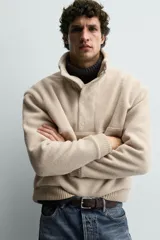 Sudadera de corte relajado confeccionada en tejido con textura de borreguillo, con cuello subido y cierre frontal de botones a presión. Presenta puños y ruedo con acabado en rib.