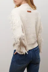 Buzo de punto color beige con cuello redondo, mangas largas con flecos decorativos y diseño de trenzas en el frente.