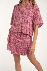 Camisa de manga corta con estampado abstracto en tonos rosa y borgoña. Tiene cuello camisero, cierre frontal con botones y corte oversize.