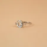 Anillo solitario de oro blanco 18k con una piedra central de aguamarina en corte ovalado y pequeños brillantes laterales engarzados en cuatro puntas.