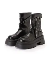 Bota biker de caña media en color negro, confeccionada en material sintético con acabado brillante. Presenta una suela chunky dentada de gran volumen, puntera redondeada y un diseño de tiras cruzadas con ojales metálicos y hebilla ajustable en la parte superior.