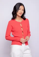 Top de tejido de punto color coral, con cuello redondo, mangas largas y cut outs frontales con botones metálicos.