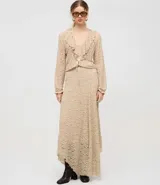 Blusa tipo bata de encaje texturizado color beige, con escote en V, mangas largas y volados aplicados en el escote. Presenta cierre frontal con botones y lazo de ajuste en la cintura.