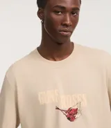 Remera de algodón color beige, corte comfort, con cuello redondo y manga corta. Presenta un gran estampado trasero de un águila con alas abiertas, sosteniendo una cinta roja con el texto "DESTRUCTION FOR APPETITE" y el logo de Guns N' Roses en la parte superior.