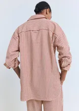Camisa de corte recto y diseño a rayas verticales en tonos terracota y blanco, con cuello camisero, cierre frontal de botones y mangas largas con puños abotonados.
