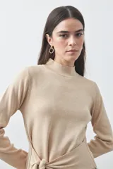 Polera de tejido de punto color beige, con cuello alto, manga larga y detalle de lazo ajustable en la cintura que aporta estructura a la silueta.