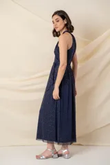 Vestido largo de tul azul marino con destellos dorados, escote halter cruzado y drapeado, con corte en la cintura y falda amplia.