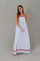 Vestido largo de algodón tipo muselina con diseño de rayas celestes y blancas. Presenta corte amplio, escote recto con tirantes finos rojos regulables y detalles de líneas rojas en el borde superior y en el ruedo.