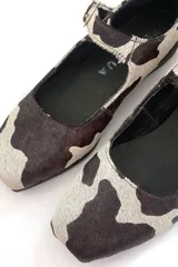 Zapato Mary Jane con estampado de vaca en blanco y negro, con correa al tobillo y hebilla plateada.