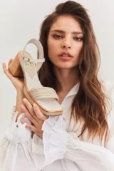 Sandalias de taco cuadrado medio, con base y talón en gamuza color tostado. Presenta una tira frontal de múltiples bandas doradas y una pulsera al tobillo con hebilla metálica.