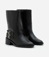 Bota de caña corta marca Satinato, confeccionada en poliuretano color negro. Presenta punta redondeada, taco bloque bajo y dos tiras decorativas con hebillas metálicas en el lateral externo.