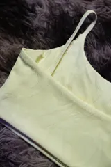 Top deportivo color amarillo claro con textura sutil y logo de la marca en color lila.