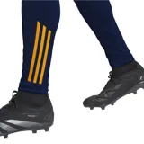 Calza deportiva azul marino de poliéster reciclado, con tecnología Aeroready, corte ajustado, cintura elástica con cordón, bolsillos laterales, puños con cremallera y escudo del Real Madrid termotransferido. Presenta paneles laterales con diseño de rayas horizontales en color naranja.