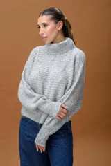 Sweater de punto con cuello alto, manga larga y diseño holgado. Presenta una textura suave con un sutil acabado brillante.