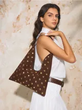 Bolso de hombro con diseño triangular, confeccionado en gamuza marrón y decorado con tachas metálicas doradas circulares en toda su superficie.