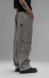 Pantalón cargo de corte oversize y silueta estructurada, confeccionado en microfibra pesada con leve elasticidad. Presenta cintura elástica con cordón de ajuste externo, cierre frontal con botón metálico, bolsillos laterales y bolsillos cargo de gran tamaño con tapa y broches a presión.