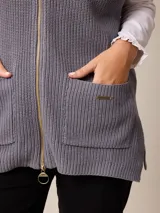 Chaleco de tejido de punto en color gris, con cierre frontal completo, cuello alto y dos bolsillos delanteros tipo parche.