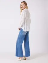 Camisa de gasa ligera y traslúcida, color blanco, con intrincados bordados búlgaros y motivos botánicos distribuidos en toda la prenda. Presenta una guarda bordada que recorre la línea de botones, el ruedo y los puños. Tiene cuello con solapa y abertura central con botones. La silueta es amplia y relajada, con mangas largas y un canesú en la espalda para una caída impecable.