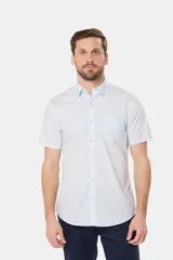 Camisa lisa de manga corta color crema, confeccionada en 100% algodón, con cuello abotonado y un bolsillo en el pecho.