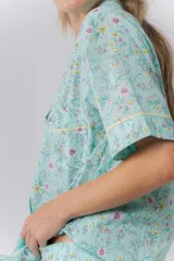 Pijama de algodón estampado con flores en tonos pastel sobre fondo verde menta. Incluye una camisa de manga corta abotonada con cuello solapa y un short con elástico en la cintura, ambos con detalles de picot en los bordes.