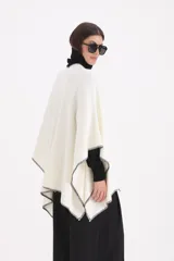 Spolverino abierto de corte amplio, color blanco con bordes en contraste de costura negra. Presenta un diseño envolvente tipo capa con mangas integradas.