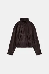 Chaqueta bomber color marrón oscuro con efecto ante, cuello subido y manga larga con puños. Tiene bolsillos delanteros, bajo con pliegues y volumen, forro interior y cierre frontal con cremallera y botones a presión ocultos.