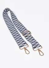 Correa de poliéster con estampado de líneas geométricas en blanco y azul marino, herrajes dorados y mosquetones en los extremos.