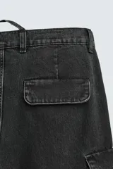 Pantalón cargo de denim lavado negro, corte relajado y tiro medio. Presenta múltiples bolsillos cargo con solapa y detalle de cierre en las perneras, además de bolsillos de vivo traseros. El bajo es ajustable con trabilla.