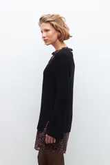 Sweater negro de tejido de punto grueso, con escote en V y detalle de cinta estampada floral en el borde del escote.