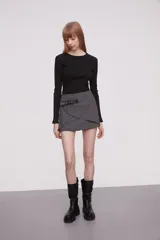 Minifalda gris de corte cruzado con detalle de cinturón lateral en cuero sintético negro con hebilla metálica.